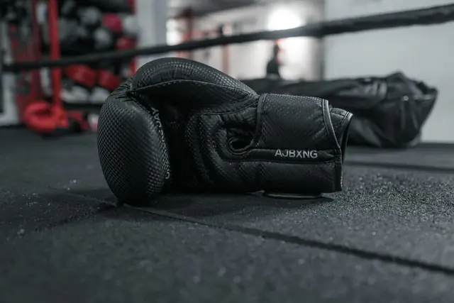 Guantes de boxeo negros apoyados sobre la lona de un ring