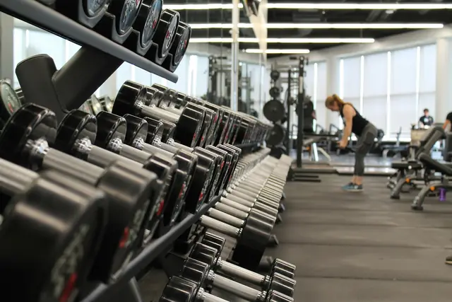 Hilera de mancuernas ordenadas en su soporte con la sala de entrenamiento al fondo
